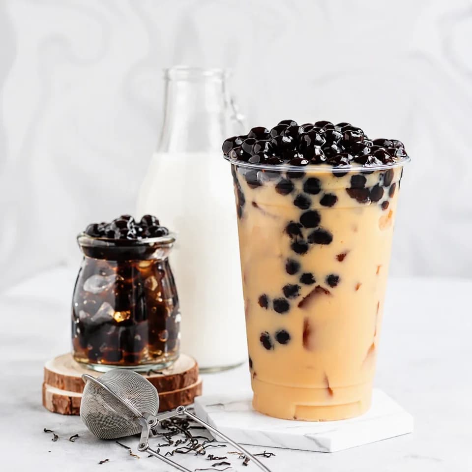 Enhanced pearl milk tea beside a jar of pearls and a milk bottle on a light surface